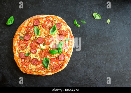 Pizza italienne avec des tomates, de salami, fromage, olives vertes et les feuilles de basilic, vue du dessus sur noir. Des pizzas fraîches, copiez l'espace. Banque D'Images