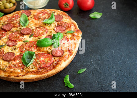 Pizza italienne avec des tomates, de salami, fromage, olives vertes et les feuilles de basilic, Close up. Des pizzas fraîches, copiez l'espace. Banque D'Images
