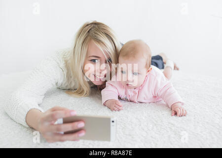 Funny baby girl make sur téléphone mobile et selfies situées près de sa mère. Nouveau-regardant la caméra et sourit. Banque D'Images