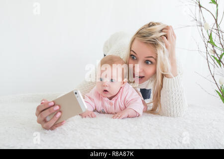 Funny baby girl make sur téléphone mobile et selfies situées près de sa mère. Nouveau-regardant la caméra et sourit. Banque D'Images