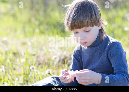 Un enfant est assis et pense. Garçon rêver sur l'herbe et triste. Banque D'Images