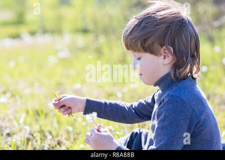 Un enfant est assis et pense. Garçon rêver sur l'herbe et triste. Banque D'Images