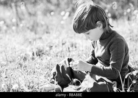 Un enfant est assis et pense. Garçon rêver sur l'herbe et triste. Banque D'Images