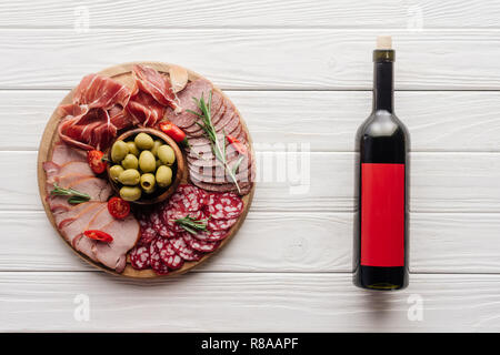 Vue de dessus de bouteille de vin rouge et d'un assortiment de collations de viande sur une table en bois blanc Banque D'Images