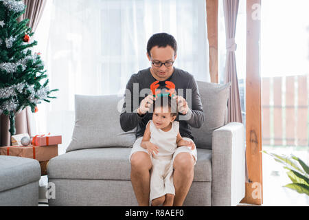 Portrait du père a aidé une petite fille portant des serre-tête de cerf dans le salon Banque D'Images