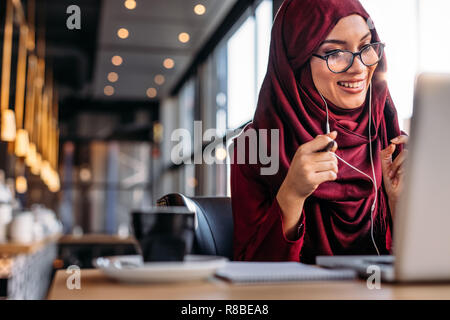 Smiling femme musulmane ayant une conversation vidéo sur ordinateur portable à la cafétéria. Freelancer femelle assis à un café et faire video appel à l'aide d'écouteurs et coffre Banque D'Images