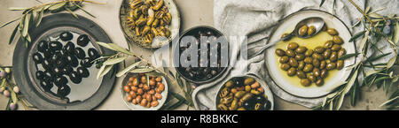 Télévision-laïcs de divers types d'olives marinées méditerranéenne dans les assiettes et bols et olivier branches sur fond de table de béton gris, vue du dessus, w Banque D'Images