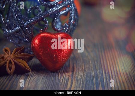 Chocolat en forme de coeur rouge et anis étoile située à boule de noël assis sur surface weathered wood background with copy space. Banque D'Images