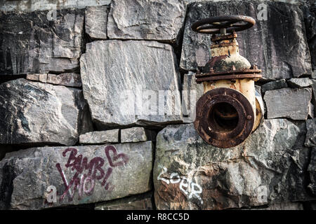 Rusty old vintage vanne en mur de pierre de graffitis griffonnés sur elle. Meubles anciens, art de rue, art déco, graffity et concepts de l'industrie. Banque D'Images