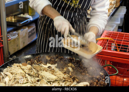 Un chef italien avec un tablier et des gants chauds cuisine risotto d'épeautre aux champignons sauvages à un Borough Market stall dans le sud de Londres Angleterre Royaume-uni KATHY DEWITT Banque D'Images