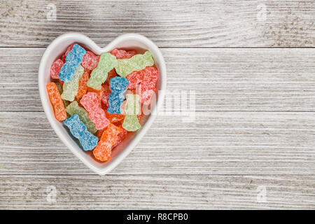 Variété de couleur différente des bonbons aigre-doux ou de la malbouffe dans un bol en forme de coeur. Banque D'Images