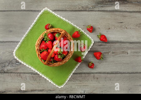 Vue sur table, petit panier plein de fraises, certains d'entre eux renversé sur la table verte chiffon sous elle. Banque D'Images