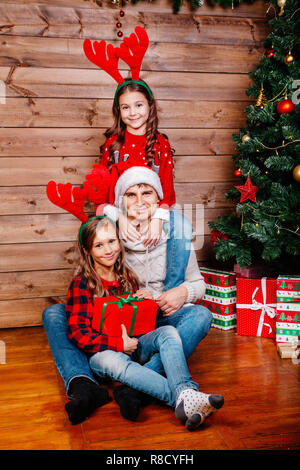 Smiling father in santa hat and daughter hugging and holding gift box près de l'arbre de Noël à la maison. Joyeux Noël et de bonnes vacances Banque D'Images