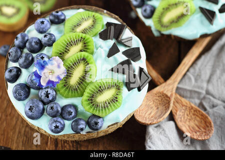 La spiruline bleu de bol, bleuets frais, kiwi et de morceaux de chocolat avec des cuillères en bois servi dans des bols de coco sur un cadre rustique backgrou Banque D'Images