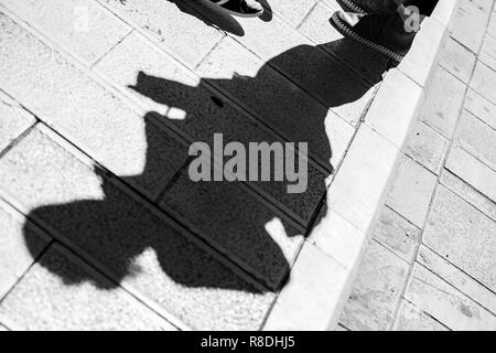 En diagonale composé photo de l'ombre d'un homme avec des chaussures de sport debout sur un patio en pierre dans la ville de Corfou en Grèce, noir et blanc Banque D'Images