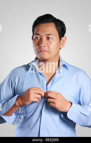 Photo image d'un beau jeune homme asiatique attrayant vinaigrette, boutonnant sa chemise bleue. Préparation de mariage. Prêts à travailler dans l'usure formelle Banque D'Images