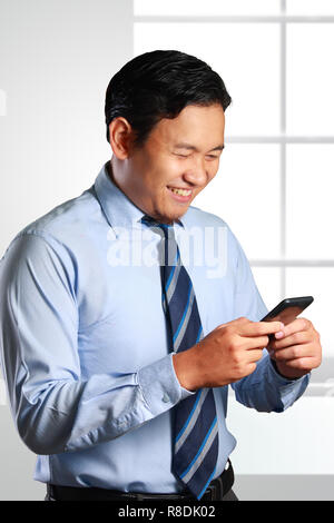 Photo image d'un beau succès attrayant Young Asian businessman smiling lors de la lecture d'information dans son smart phone Banque D'Images