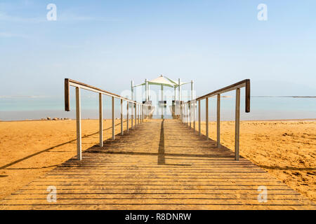 Jetée sur la plage sur la mer Morte. Ein Bokek, Israel. Chemin de bois sur le sable jaune en laissant la distance de la mer morte. Le chemin sous l'auvent à l'al. Banque D'Images