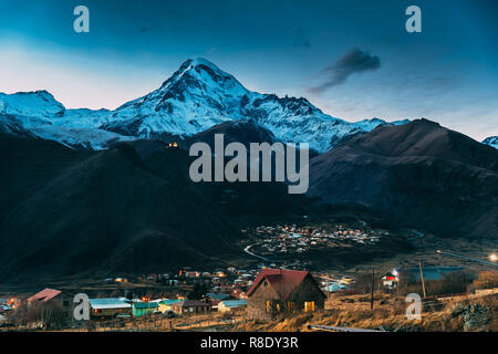 Stepantsminda, la Géorgie. Sommet du Mont Kazbek couverte de neige, célèbre église Gergeti et maisons de campagne à soir la foudre. Belle Georgian Banque D'Images