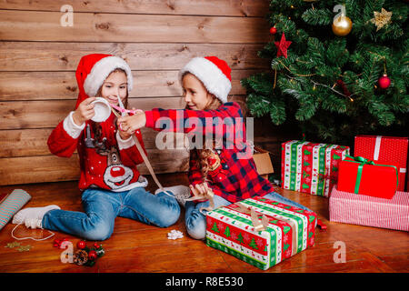 Happy funny Little Sisters dans Santa hats cadeaux pack near Christmas Tree Banque D'Images