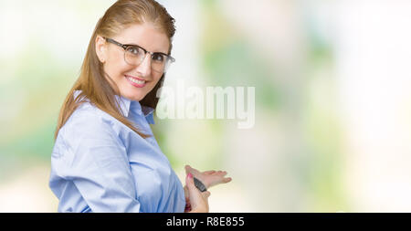 Belle maturité d'âge moyen business woman wearing glasses sur fond isolé invitant à entrer smiling natural avec main ouverte Banque D'Images