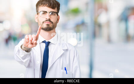 Jeune scientifique professionnel homme portant un manteau blanc fond isolé au pointage du doigt vers le haut et l'expression de colère Banque D'Images