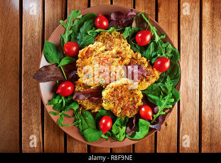 Des burgers de légumes Pommes de terre et les lentilles, servi sur une assiette avec des tomates et de la salade verte sur un fond de bois ; vue d'en haut. Banque D'Images