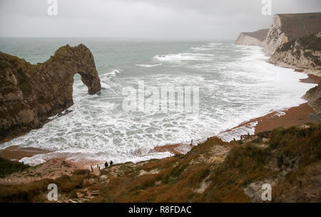 Les gens sur la plage regarder les vagues déferlent sur Durdle Door dans le Dorset comme amber alerte mises en garde de l'accumulation de neige et de glace ont été émis pour le nord de l'Angleterre et des Midlands. Banque D'Images