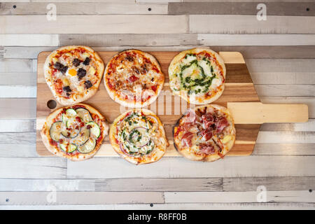 Vue aérienne de six différentes pizzas sur une planche en bois sur une table en bois Banque D'Images