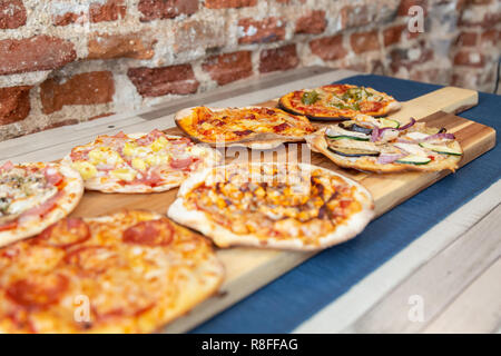 Sept petites pizzas sur une planche en bois, fraîchement sorti du four, prêt à manger sur un restaurant. avec l'accent dans les légumes de la pizza. Sur une table en bois avec un bl Banque D'Images