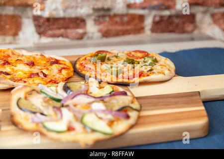 Sept petites pizzas sur une planche en bois, fraîchement sorti du four, prêt à manger sur un restaurant. Avec l'accent sur le piment de la pizza. Sur une table en bois avec un t bleu Banque D'Images