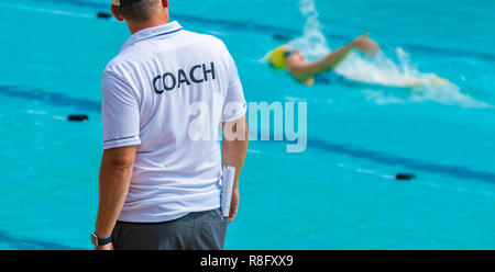 Vue arrière de l'entraîneurs de natation, le port de chemise COACH son watiching faisant dos nageur Femme at a local piscine extérieure Banque D'Images