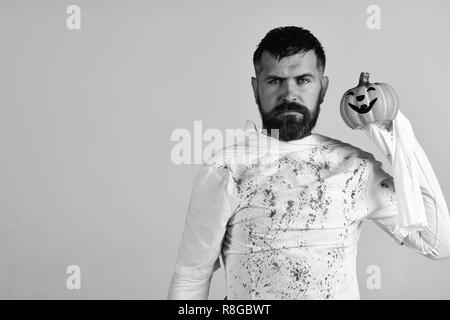 L'homme avec toute l'expression visage isolé sur fond gris, l'espace de copie. Caractère dans Halloween Costume fantôme blanc. Guy avec barbe est titulaire d'orange citrouille avec sourire. Heureux temps des Fêtes Halloween concept Banque D'Images