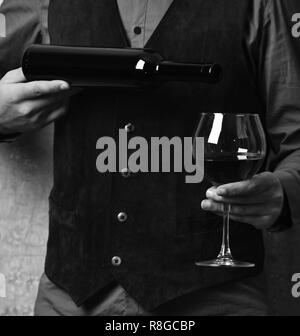 Barman sert verre à vin rouge. Garçon se verse dans un verre de vin rouge à partir de la bouteille. La main des hommes est titulaire d'une bouteille de vin sur fond mur beige. Service et boissons restaurant concept. Banque D'Images