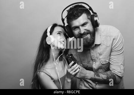 Guy avec barbe et dame avec des visages souriants de profiter de la musique. Couple in love est titulaire d'un micro, chante sur fond bleu. L'homme porte la barbe avec écouteurs, copiez l'espace. Plaisir et amusement concept Banque D'Images