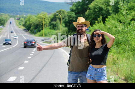 Voiture voyageurs essayent d'arrêter. L'auto-stop est l'un des moyens les moins coûteux de voyager. Auto-stoppeurs couple voyageant de l'été journée ensoleillée. Voyageurs Couple man and girl l'auto-stop au bord de la route fond nature. Banque D'Images