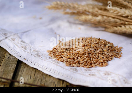 Des grains de blé sur fond blanc vintage nappes en lin. Selective focus macro shot. Ingrédients pour pain, une vieille table en bois. La vie encore rustique Banque D'Images