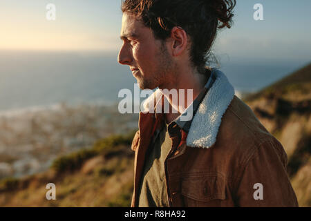 Portrait of young man wearing jacket debout sur la falaise et à la recherche à une vue. L'homme en vacances sur journée d'hiver. Banque D'Images