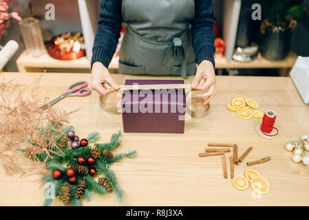 Vendeur femelle décore boîte-cadeau avec du papier d'emballage et ruban d'or, de la décoration. Femme wraps présent sur la table, le décor intérieur Banque D'Images