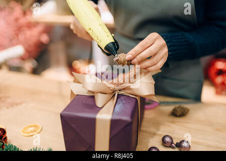 Vendeur femelle décore boîte-cadeau avec fir cone, handmade rétractable et la décoration. Femme wraps présent sur la table, le décor intérieur Banque D'Images