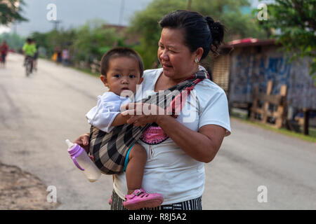 Thakhek, Laos - 20 Avril 2018 : mère tenant un enfant à la tombée de la nuit dans une rue d'un village du sud du Laos Banque D'Images