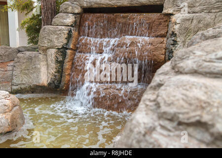 Cool l'eau claire s'écoule à travers une cascade de cascade artificielle faite de pierres. Verse de l'eau ci-dessus et formes mousses lors de tomber vers le bas Banque D'Images