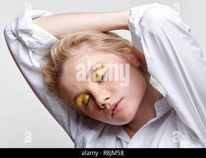 Portrait d'une jeune femme blonde en blouse blanche aux yeux clos sur fond gris. Banque D'Images