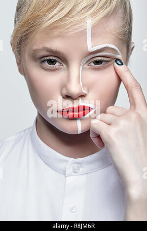 Beauty fashion portrait d'une jeune femme sur fond gris. Femme avec un peu de maquillage créatif peinture sur visage. Fille aux mains près de visage. Banque D'Images