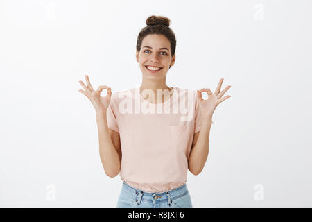 Fille heureuse tout va bien enfin soulagé et joyeux qui pose plus de souci permanent du mur gris avec orbs, montrant les choses geste ok sous contrôle, l'approbation du bon travail de team smiling at camera Banque D'Images