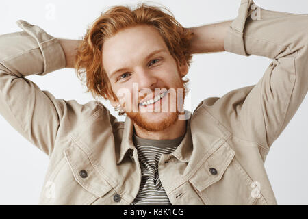 Gros plan d'adjudication mignon et sympa beau petit ami roux avec les cheveux ondulés et tête inclinable barbe tenant les mains derrière et tout sourire avec l'expression sans souci Banque D'Images