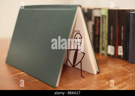 Livres sur une table en bois avec un stick figure sur un livre ouvert assis et souriant Banque D'Images
