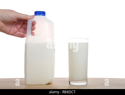 Femme main tenant la moitié gallon carton de lait sur la table en bois clair à côté de verre de lait versé isolé sur fond blanc. Banque D'Images