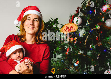 Baby Girl dressed as Santa Claus embrassé avec amour par sa mère, de protection concept de famille à Noël. Banque D'Images
