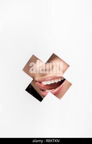 Cropped shot of young woman licking lips par trou en forme de croix sur blanc Banque D'Images